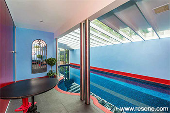 Behind the glass art wall is a tiled indoor heated swimming pool area painted in Resene Delta Blue with a glass ceiling